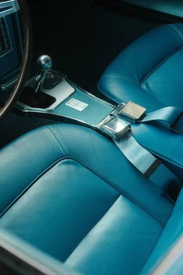 A classic car interior in turquoise leather with a chrome-buckled lap belt fastened across the seat.