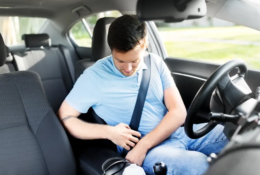 A driver fastening the seatbelt in a fleet passenger vehicle, seated at the wheel with the belt drawn across.