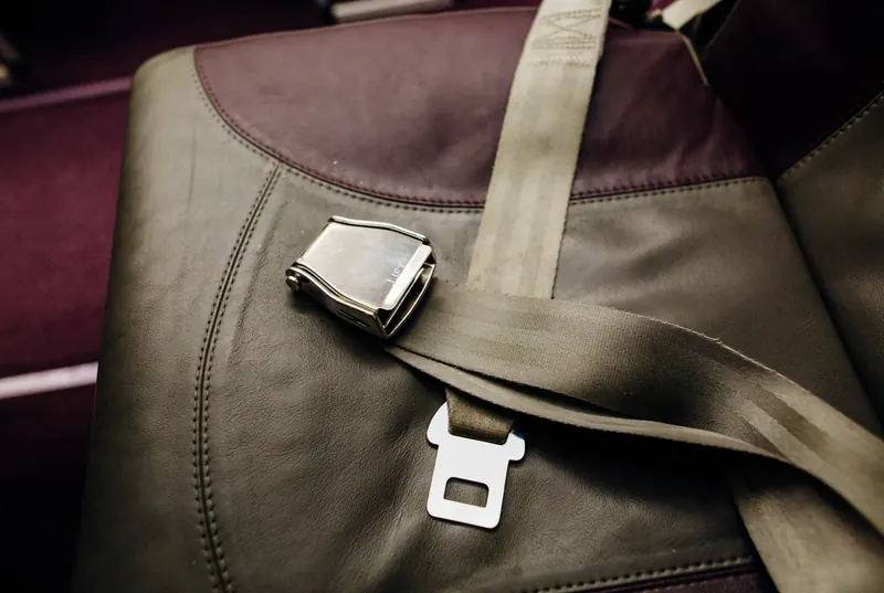 A two-point lap belt with a metal lift-latch buckle laid across a leather passenger seat.