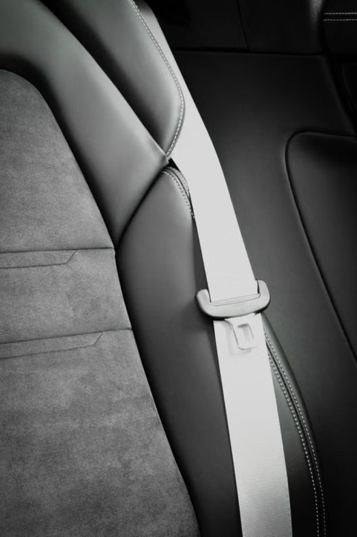 A pale seatbelt webbing strap running over a dark two-tone vehicle seat, with the shoulder guide clearly visible.