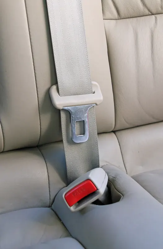 A light grey three-point seatbelt running across a leather vehicle seat with the tongue engaged in the buckle.