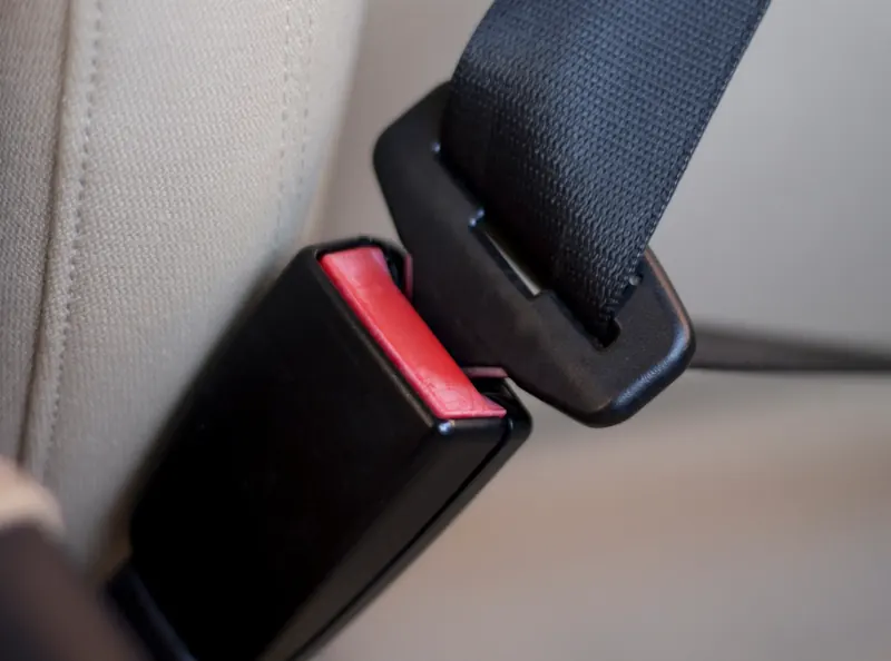 A seatbelt tongue plate positioned beside its matching buckle receiver, ready to engage, against a beige seat.